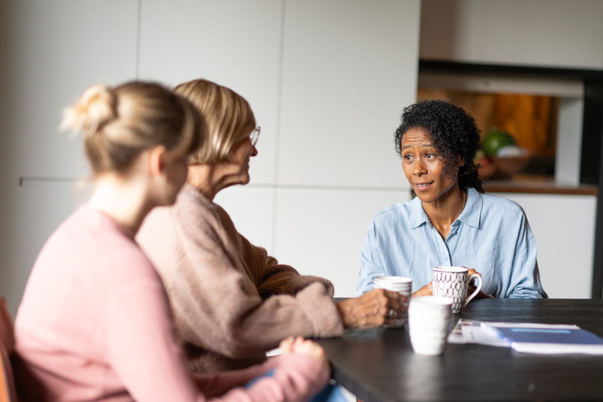 Drie personen zitten samen rond een tafel in gesprek.