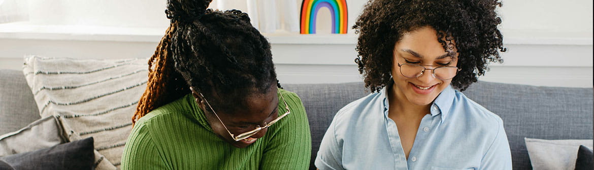 Twee personen zitten samen op een sofa en bekijken digitale documenten op een laptop, met een koffiemok en persoonlijke spullen in een huiselijke omgeving.