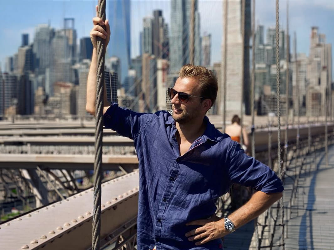 Man (Jens) psoeert op een iconische brug tijdens een zonnige dag in New York.