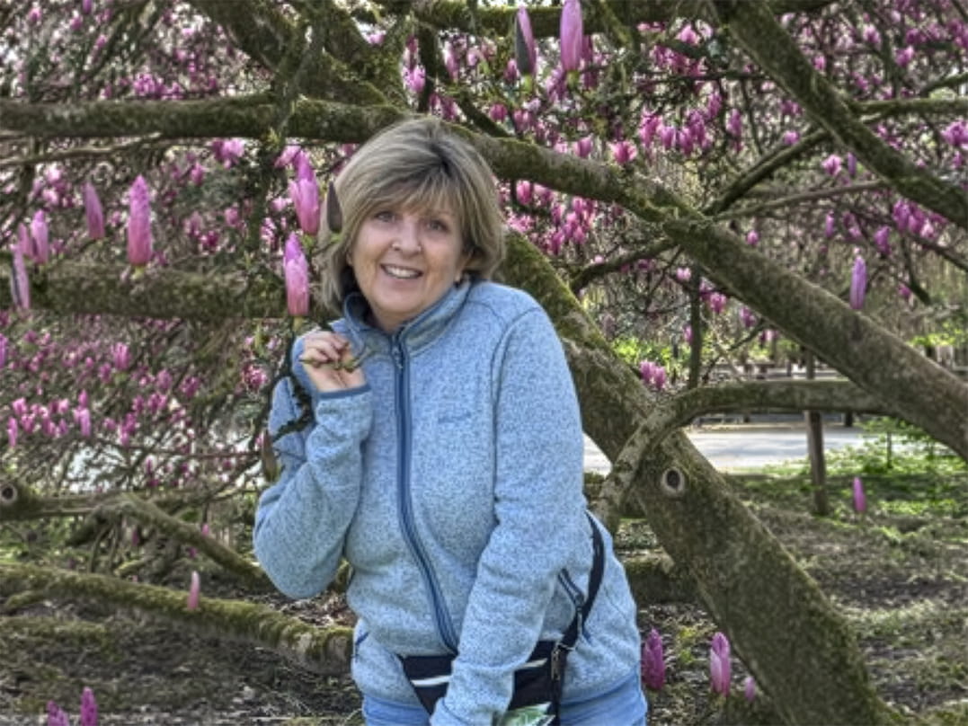 Vrouw (Katia) poseert tussen de takken van een bloeiende magnoliaboom met roze bloemen in een park.