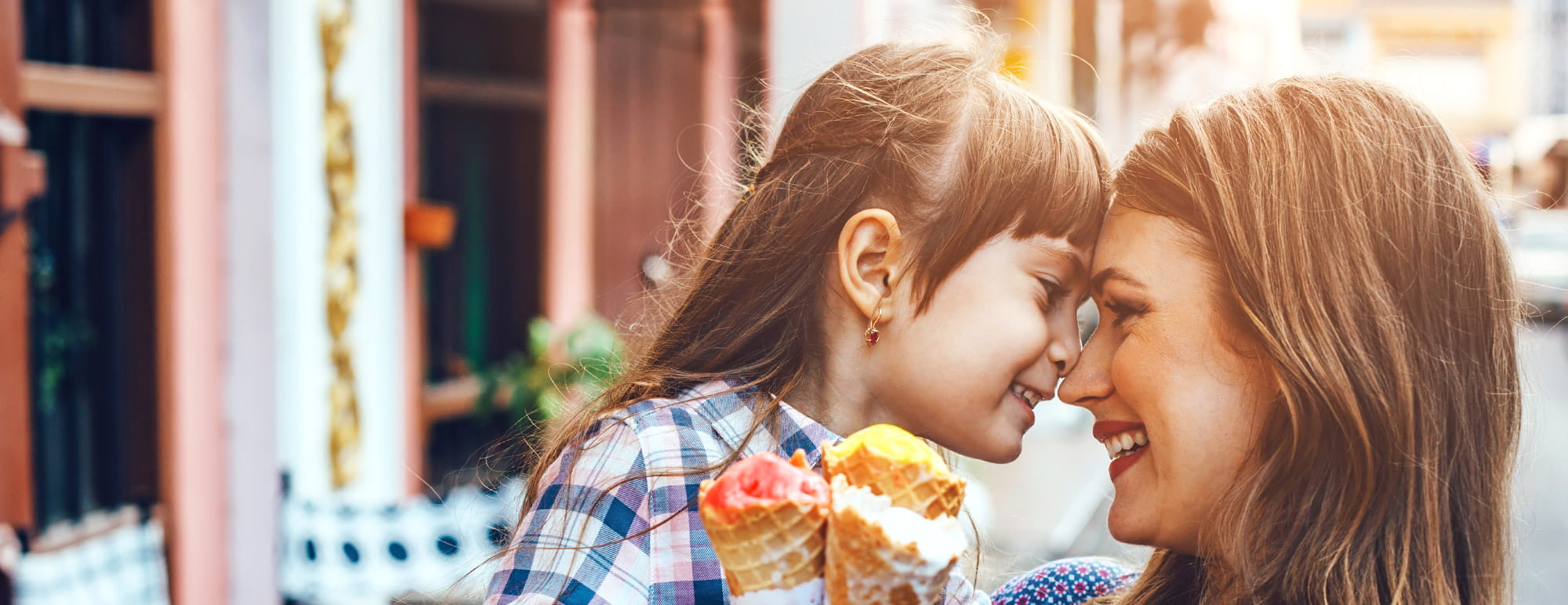 Un adulte et un enfant sont assis proches l’un de l’autre dans une rue et se touchent le nez pendant que l’enfant tient une glace.