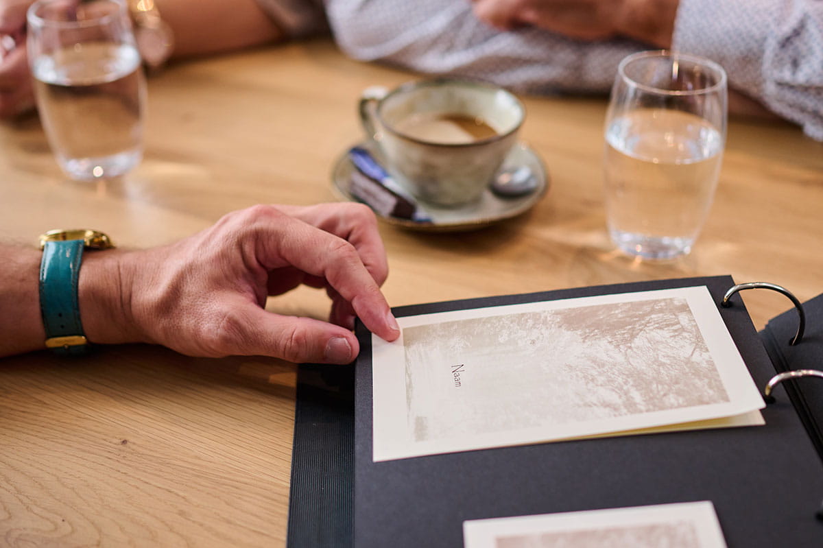 Persoon bespreekt een herinneringskaart in een map tijdens een gesprek aan tafel.
